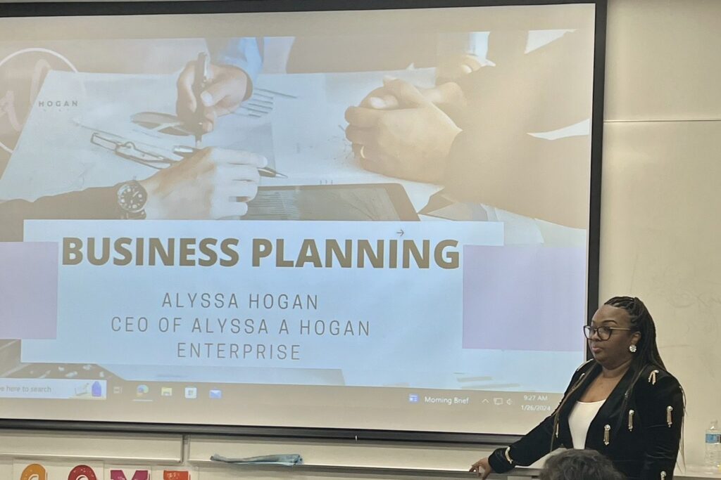 Alyssa Hogan presenting a business planning session beside her title slide