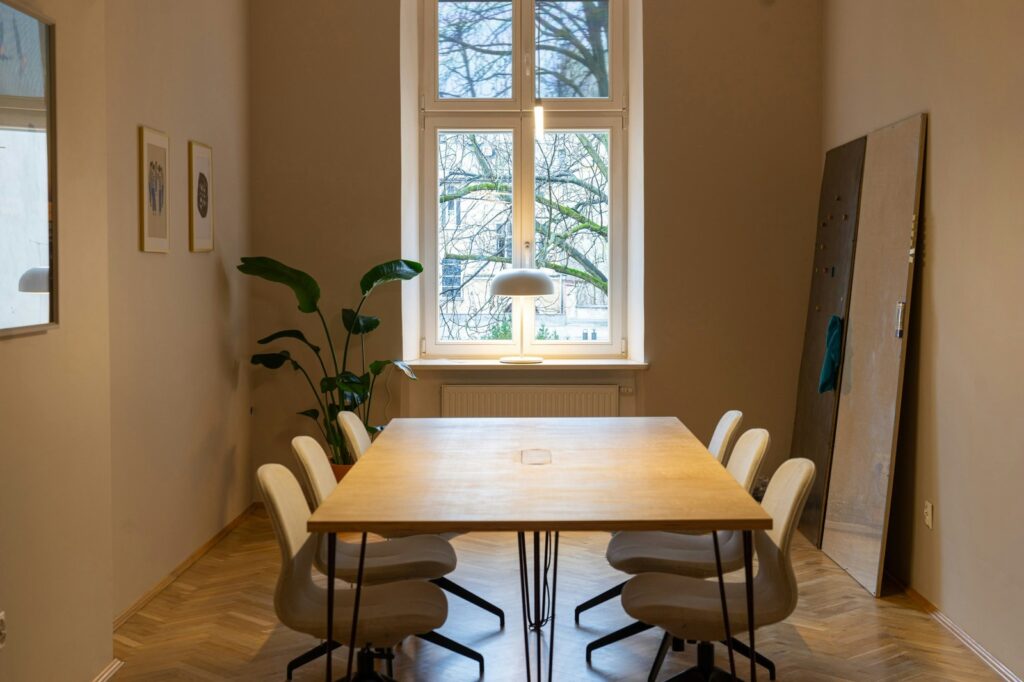 A wooden meeting table and chairs beside a tall window