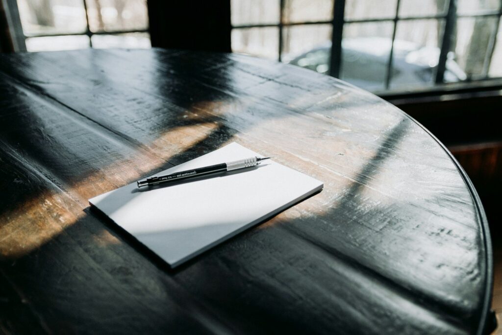 A pen and a blank notepad on a dark round table