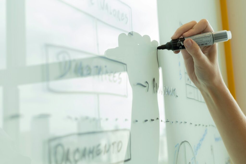 A hand drawing a diagram on a glass writing board